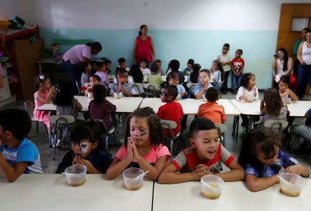 Students pray before eating their soup cooked for them during an activity for the end of the school year at the Padre Jose Maria Velaz school in Caracas, Venezuela July 12, 2016. REUTERS/Carlos Jasso