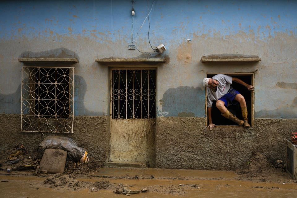 José Medina sale por la ventana de casa inundada por el desborde de un riachuelo a causa de las fuertes lluvias, el domingo 9 de octubre de 2022, en Las Tejerías, Venezuela. (AP Foto/Matias Delacroix)