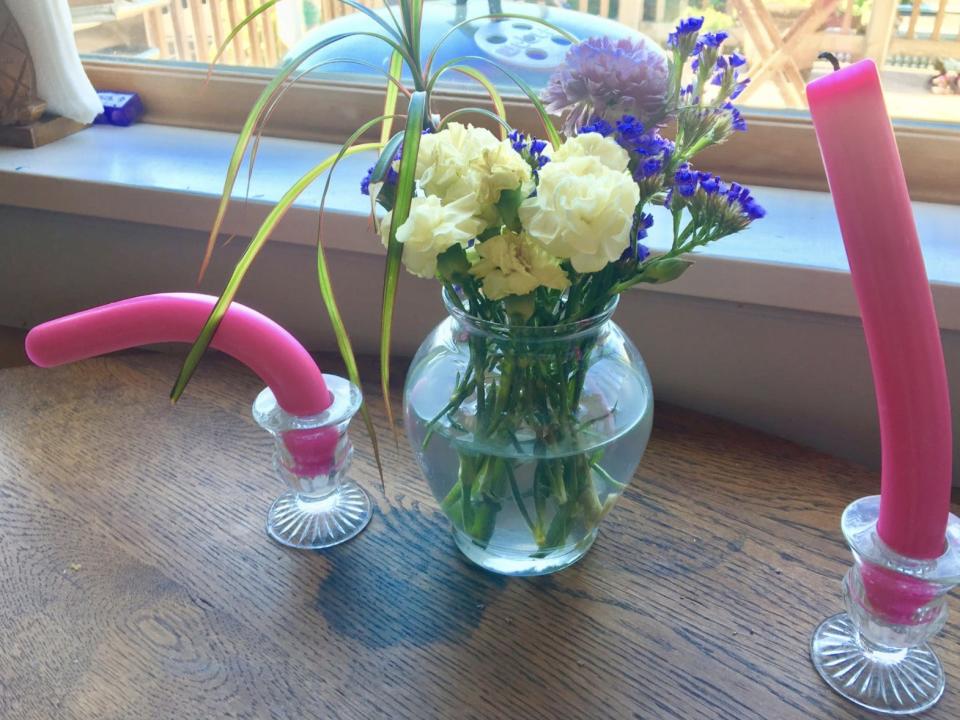 Pink dandles drooping and a vase of flowers on a wooden window-side table.