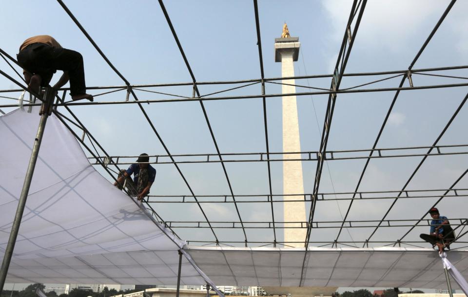 In this Thursday, May 8, 2014 photo, workers set up a tent that will be used for a weekend event as the National Monument is seen in the background in Jakarta, Indonesia. The 132-meter (433-feet) tall monument, a popular landmark in the capital, is being cleaned for the first time in more than two decades. (AP Photo/Dita Alangkara)