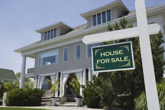 Three-story house on a clear day with for-sale sign highlighted.