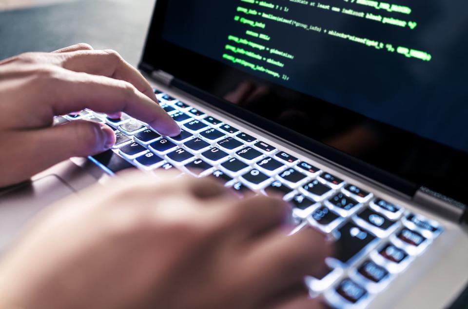 A stock photo shows a hacker typing in code on a laptop computer.
