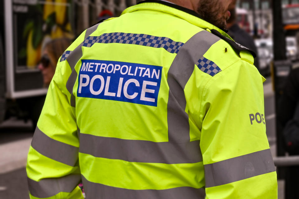 London, England - August 2021: Rear view of a Metropolitan Police officer wearing a reflective jacket. In the background are crowds of people.