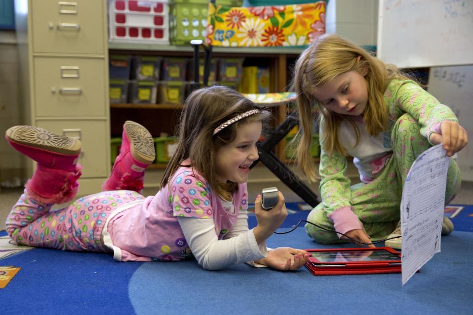 This photo taken Nov. 25, 2013 shows Josie Barton, 7, left, recording audio into an iPad for an iMovie project with classmate Marin Peale, 7, in their multi-grade first and second grade class at Jamestown Elementary School in Arlington, Va. Needed to keep a school building running these days: Water, electricity _ and broadband. Interactive digital learning on laptops and tablets is, in many cases, replacing traditional textbooks. Students are taking computer-based tests instead of fill-in-the bubble exams. Teachers are accessing far-off resources for lessons. (AP Photo/Jacquelyn Martin)