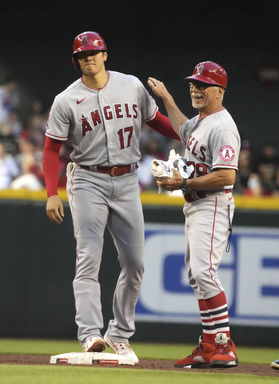 Los Angeles Angels' Shohei Ohtani (17) laughs with first base coach Bruce Hines after hitting an RBI-double against the Arizona Diamondbacks in the third inning during a baseball game, Friday, June 11, 2021, in Phoenix. (AP Photo/Rick Scuteri)