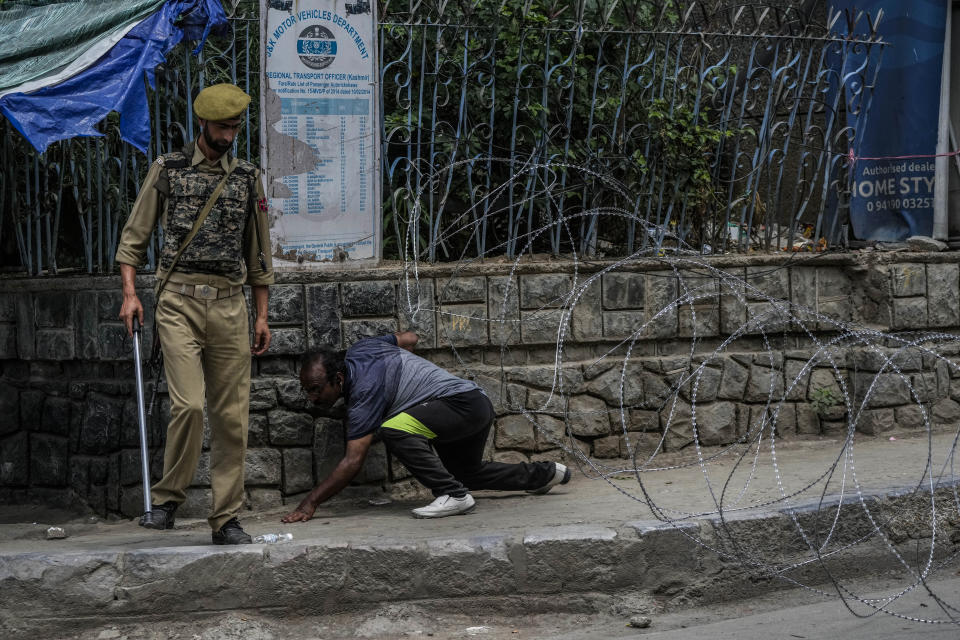 A Kashmiri man crosses barbed wire set up by police as a roadblock during restrictions in Srinagar, Indian controlled Kashmir, Sunday, Aug. 7, 2022. Authorities had imposed restrictions in parts of Srinagar, the region's main city, to prevent gatherings marking Muharram from developing into anti-India protests. (AP Photo/Mukhtar Khan)