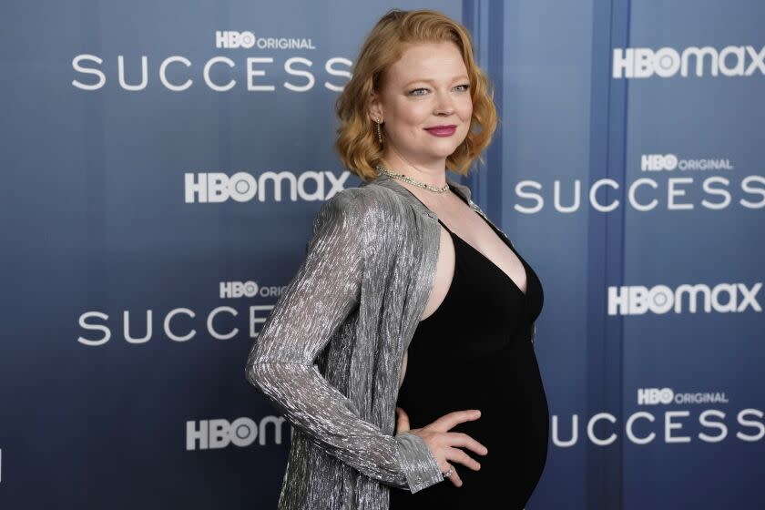 A pregnant woman with short red hair posing with her hands on her hips in a tight black dress and silver shrugg