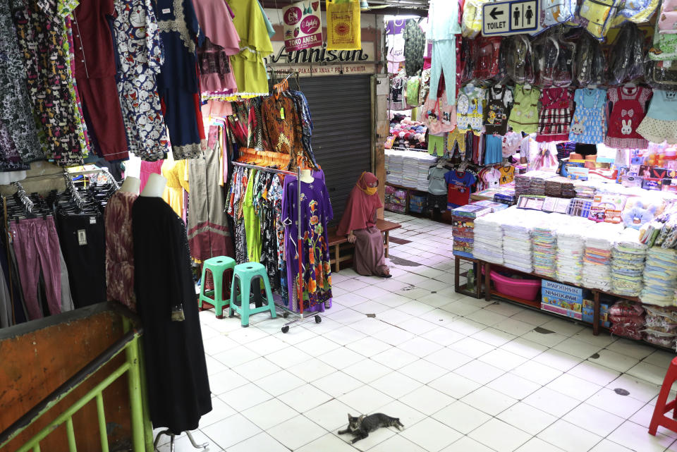 A clothes seller waits for costumers at a quiet market in Jakarta, Indonesia, Friday, April 10, 2020. Authorities began stricter measures to halt the new coronavirus' spread in Indonesia's capital Friday, with its normally congested streets empty after death toll spiked in the past week. (AP Photo/Achmad Ibrahim)