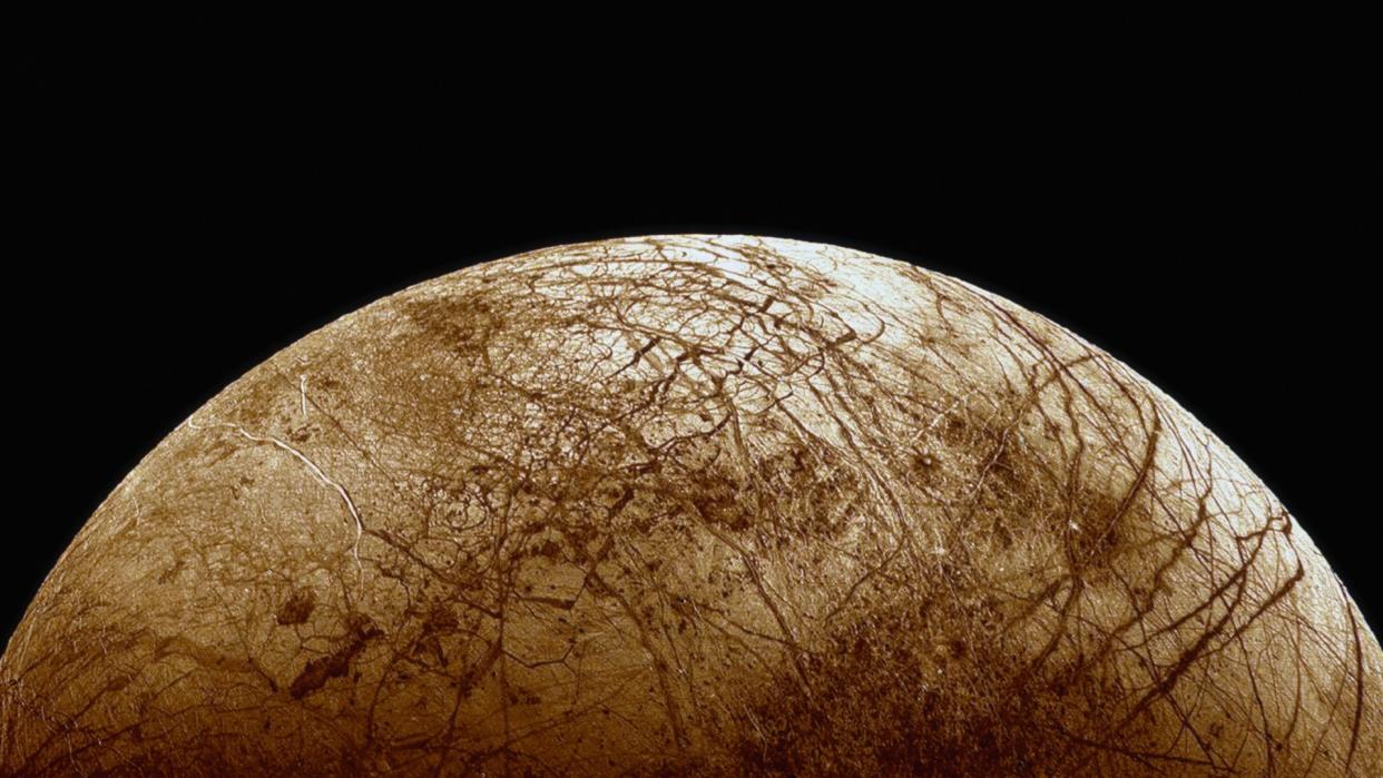  an illustration of Jupiter's icy moon Europa. it is an orangeish orb covered in deep cracks 