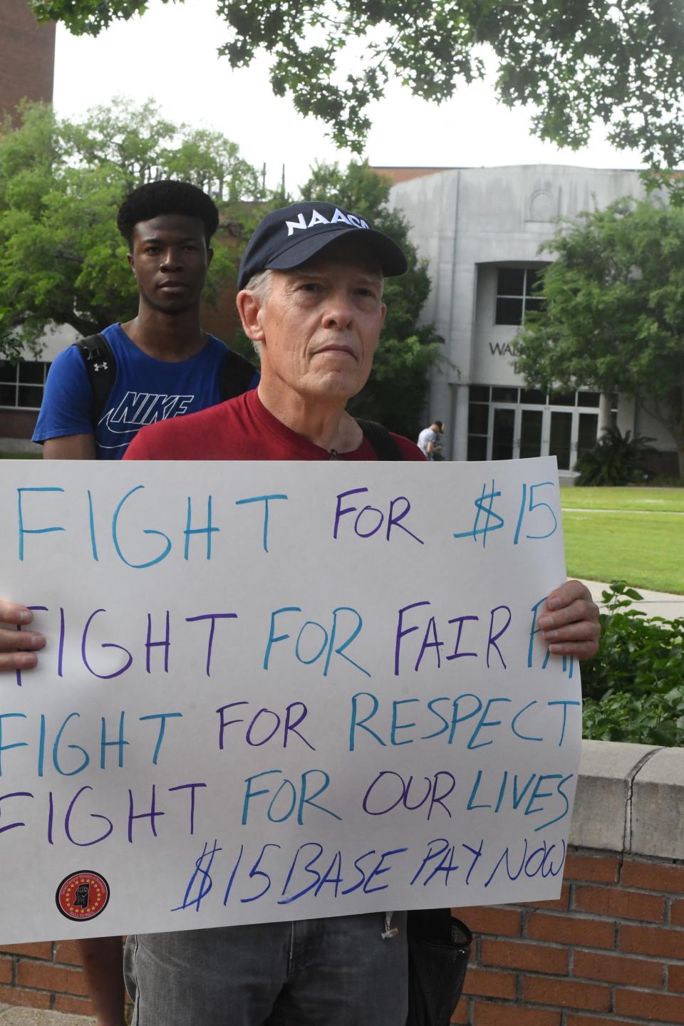 Stephen Judd, a professor at the University of Southern Mississippi, holds a sign during a rally at the Hattiesburg, Miss., campus, Thursday, May 5, 2022. Rally participants are seeking a higher minimum wage for university employees.