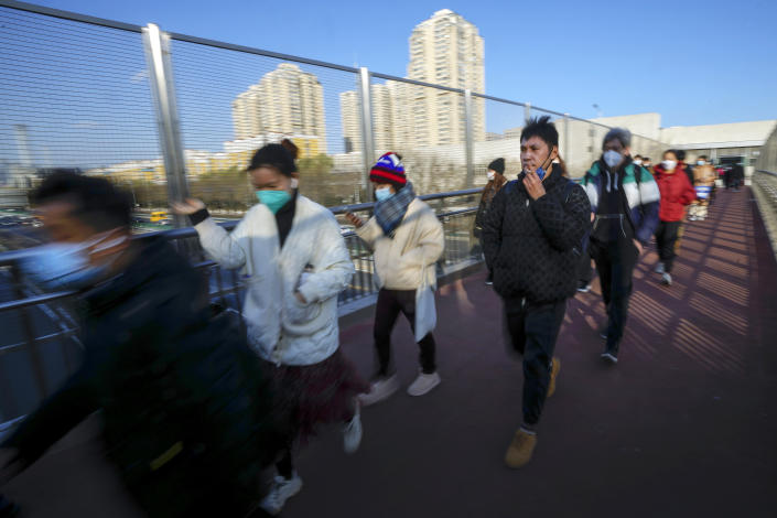 A man smokes as masked commuters walk along a pedestrian bridge in Beijing, Thursday, Dec. 8, 2022. China is the last major country still trying to stamp out transmission of the virus while many nations switch to trying to live with it. As they lift restrictions, Chinese officials have also shifted to talking about the virus as less threatening — a possible effort to prepare people for a similar switch. (AP Photo/Andy Wong)