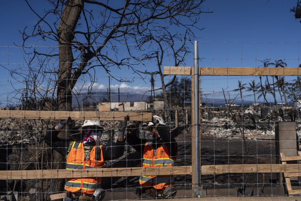 Two workers put up a fence along a residential area destroyed by a deadly wildfire in Lahaina, Hawaii, Saturday, Aug. 19, 2023. (AP Photo/Jae C. Hong)