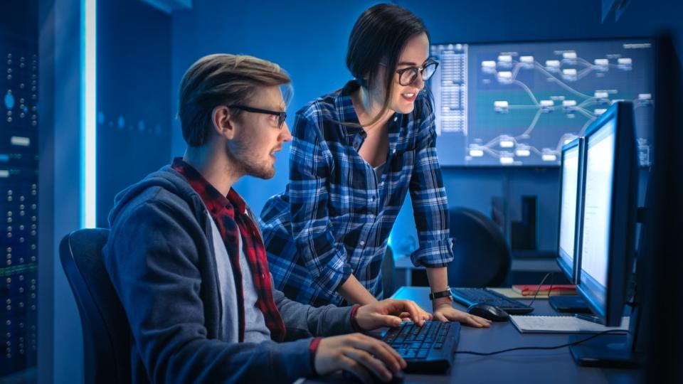 Two cybersecurity workers at their monitors analyzing data.