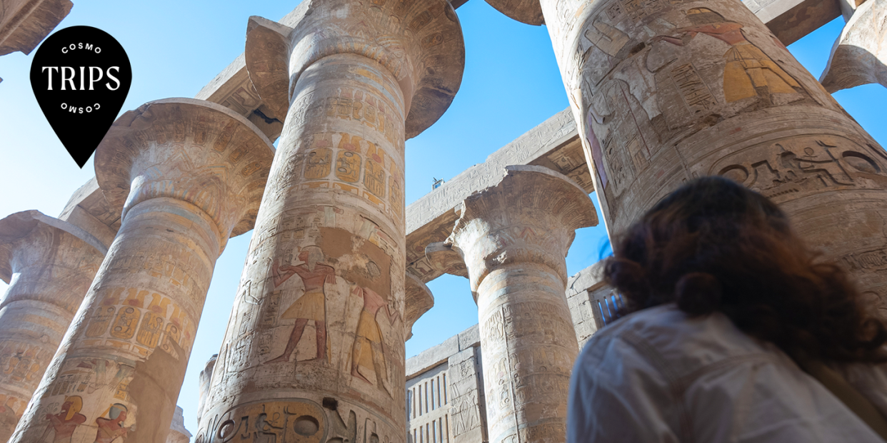 a woman stands in a temple looking up at painted pillars, with the words cosmo trips over it