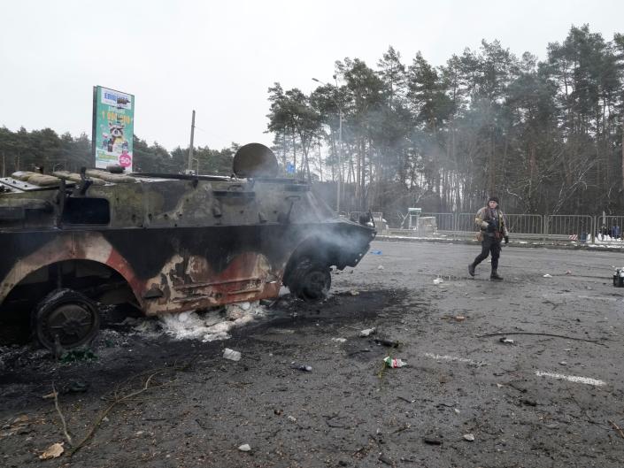 A volunteer of Ukraine&#39;s Territorial Defense Forces walks by a damaged armored vehicle at a checkpoint in Brovary, outside Kyiv, Ukraine, Tuesday, March 1, 2022