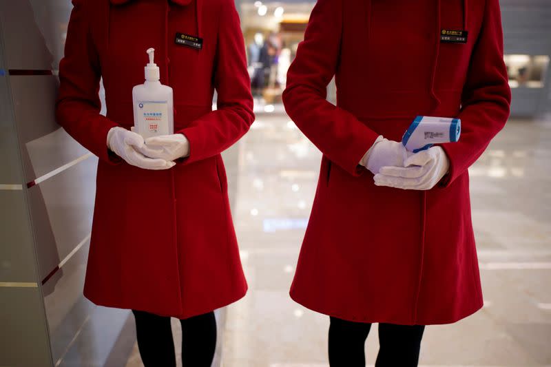 Staff members holding disinfectant gel and thermometer are seen at an entrance of a shopping mall in Wuhan