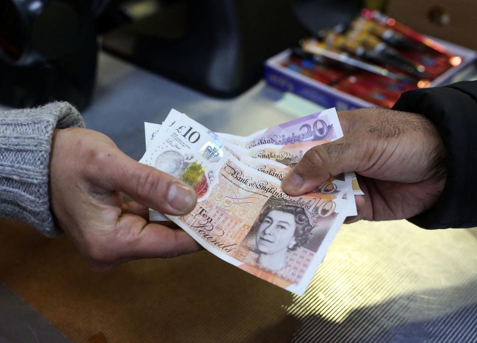 A shopkeeper (L) passes a customer their change in GBP pound sterling ten and twenty pound notes, at a shop in east London on March 31, 2023. (Photo by Susannah Ireland / AFP) / TO GO WITH AFP STORY BY Akshata KAPOOR (Photo by SUSANNAH IRELAND/AFP via Getty Images)