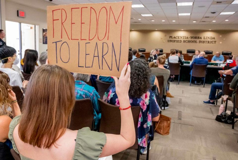 A student holds up a sign that says "freedom to learn" as the school board discusses banning critical race theory