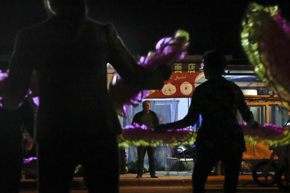 In this Sept. 20, 2018, photo, an Uighur man, center, watches Han Chinese dance in front of restaurants and shophouses operated by Uighur people at the Unity New Village in Hotan, in western China's Xinjiang region. While thousands of Uighur Muslims across China’s Xinjiang region are forced into re-education camps, China’s fledgling vision for ethnic unity is taking shape in a village where Han Chinese work and live alongside Uighur minorities. (AP Photo/Andy Wong)