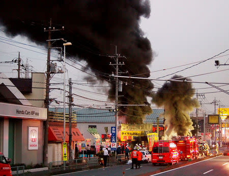 Firefighters gather around black smoke spewing from an unmanned underground cable facility in Niiza, Saitama prefecture, Japan October 12, 2016. Kyodo/via REUTERS