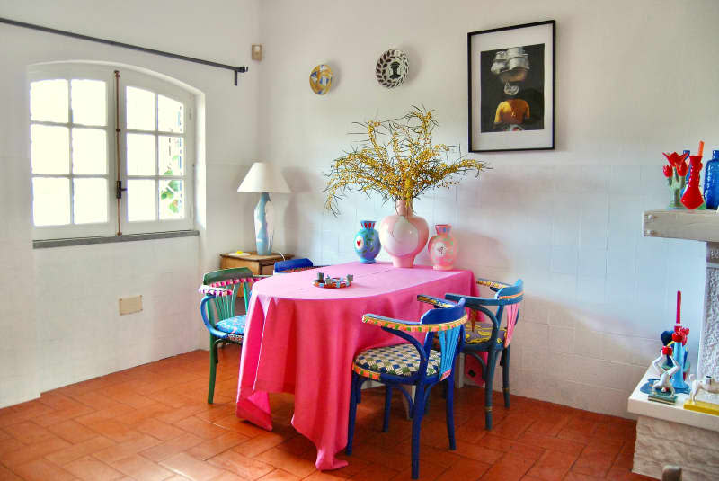 Colorful chairs at table with pink tablecloth in dining area with white walls.