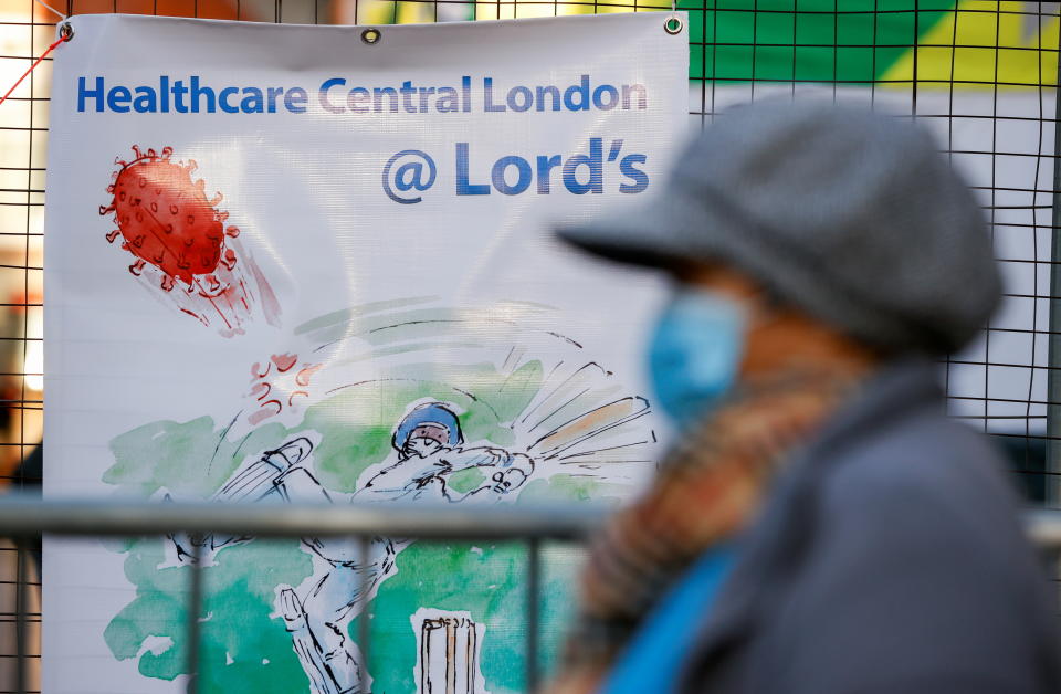 A person wearing a protective mask walks past a banner advertising vaccination at Lord's Cricket Ground, amid the outbreak of the coronavirus disease (COVID-19) in London, Britain, January 22, 2021.  REUTERS/John Sibley