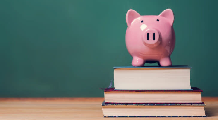 A pink piggy bank sitting on three stacked textbooks with a green chalkboard in the background.