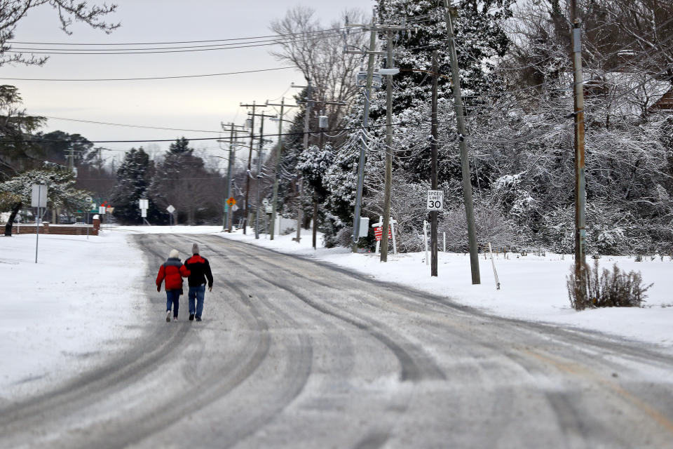 People walk through the snow along West County Street in Hampton, Va., Saturday, Jan. 22, 2022. A layer of ice and a blanket of snow has covered coastal areas stretching from South Carolina to Virginia. The winter weather system that entered the region on Friday brought colder temperatures and precipitation not often seen in the region. (Jonathon Gruenke/The Virginian-Pilot via AP)