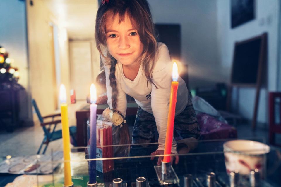 Little girl lighting menorah at home