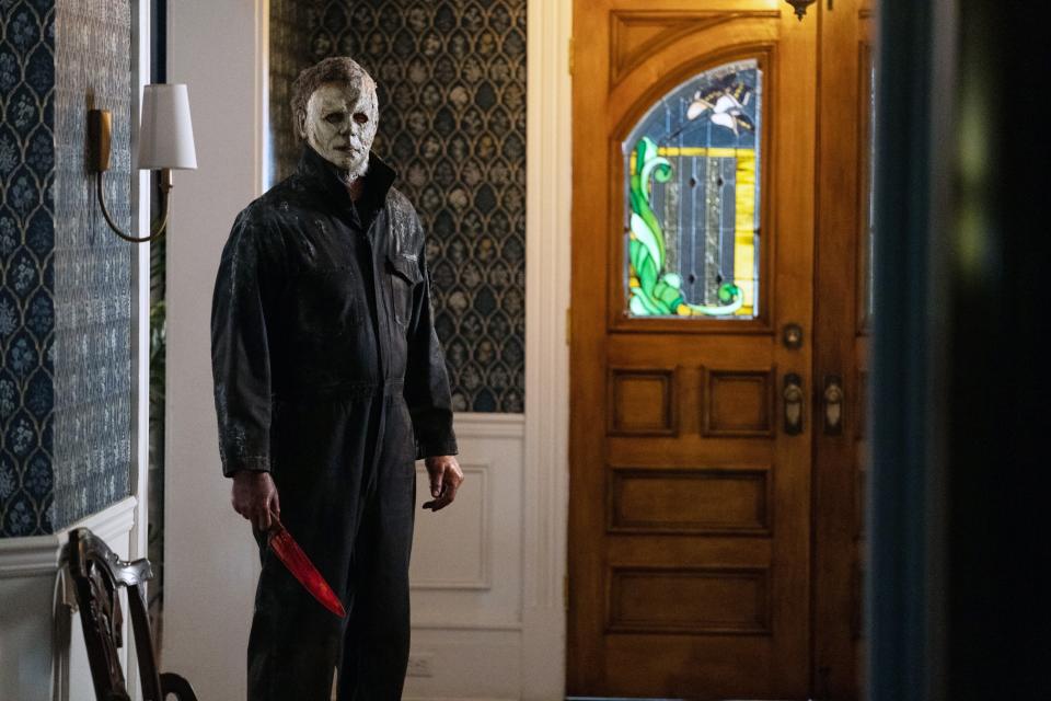 Michael Myers holding a knife and standing by a door in a hallway