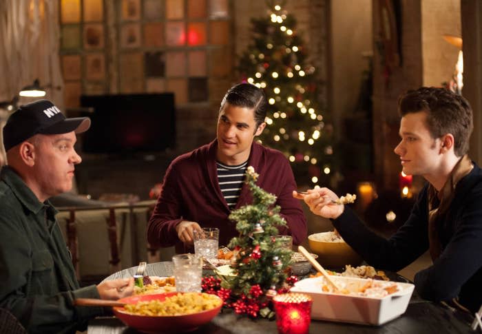 Mike O'Malley, Darren Criss, and Chris Colfer are sitting at a dinner table decorated for Christmas, sharing a meal