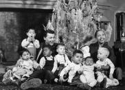 <p>Josephine Baker wears a simple black belted dress in front of the tree in her French Chateau, with some of her adopted children and her husband, Jo Bouillon.</p>