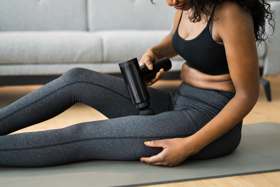 Woman wearing activewear and using a massage gun on her leg