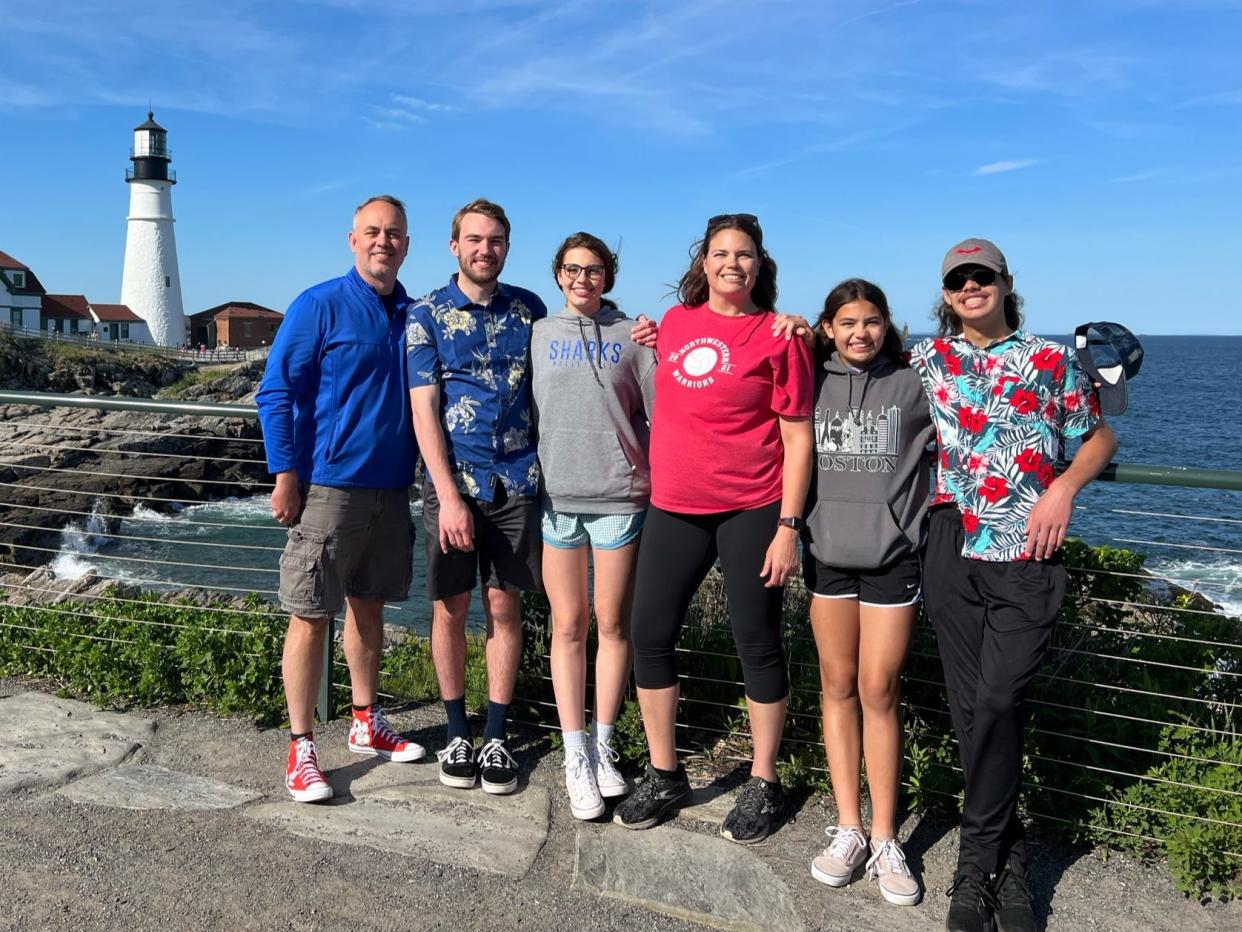 Luke Macy with his family standing in front of the ocean and a lighthouse.