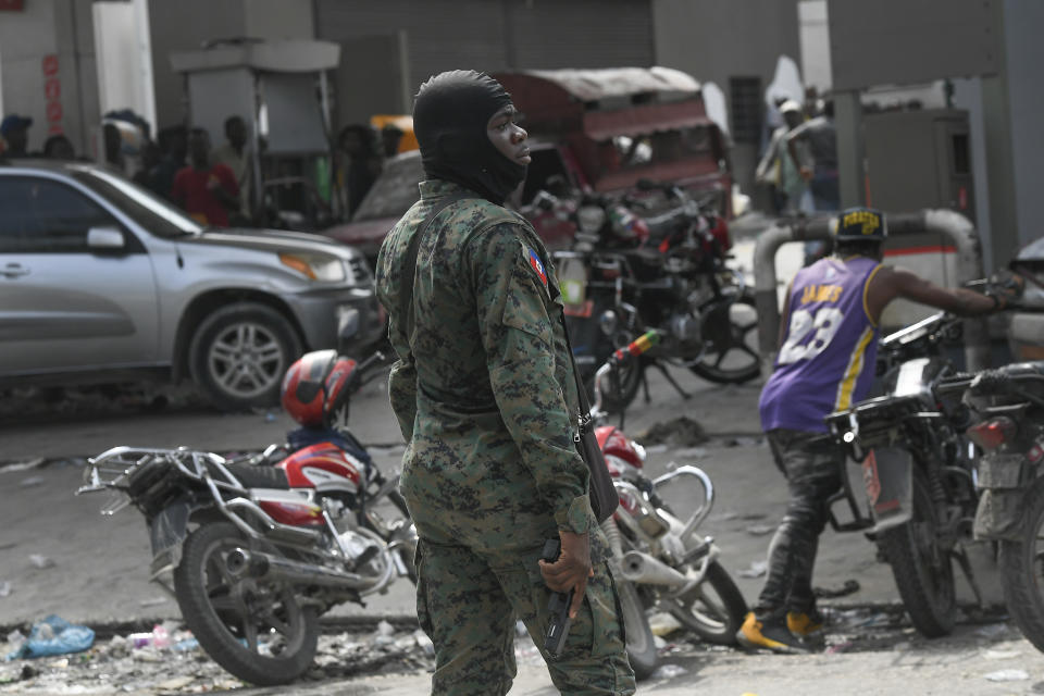 An armed police officer stands outside a gas station after police shot bullets into the air to disperse a crowd threatening to burn down the gas station because the crowd believed the station was withholding gas, in Port-au-Prince, Haiti, Saturday, Oct. 23, 2021. The ongoing fuel shortage has worsened, with demonstrators blocking roads and burning tires in Haiti's capital to decry the severe shortage and a spike in insecurity. (AP Photo/Matias Delacroix)