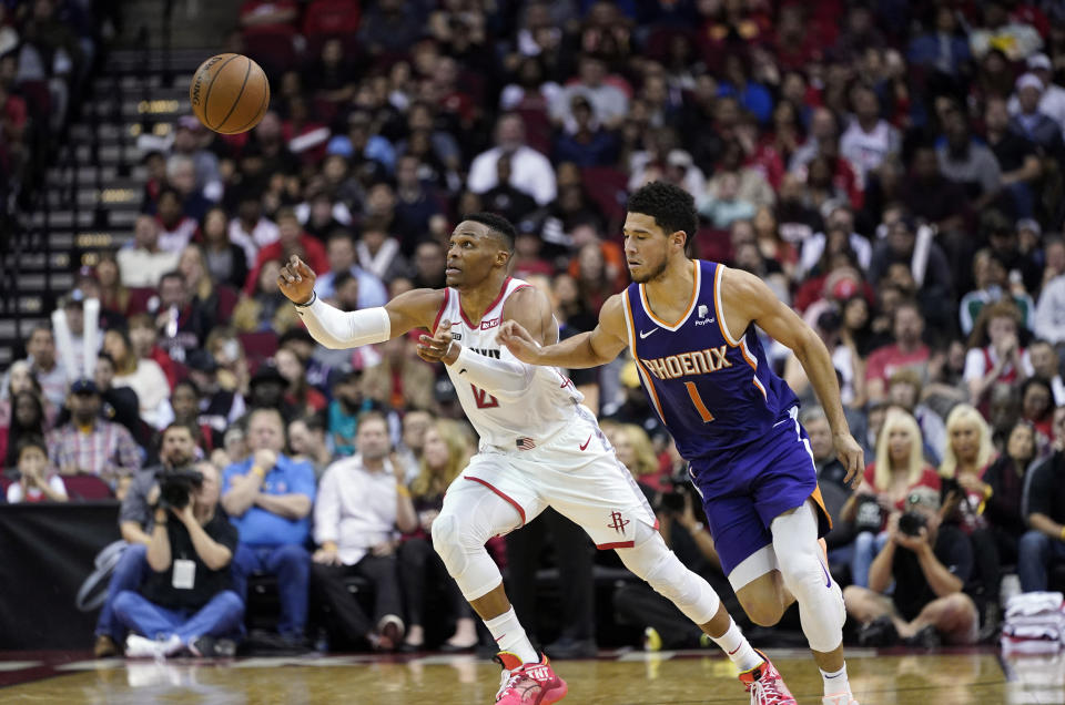 Houston Rockets' Russell Westbrook (0) and Phoenix Suns' Devin Booker (1) reach for a loose ball during the first half of an NBA basketball game Saturday, Dec. 7, 2019, in Houston. (AP Photo/David J. Phillip)