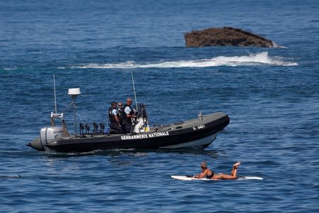 A surfer looks at French gendarmes on a boat as they patrol the coast ahead of the G7 summit in Biarritz