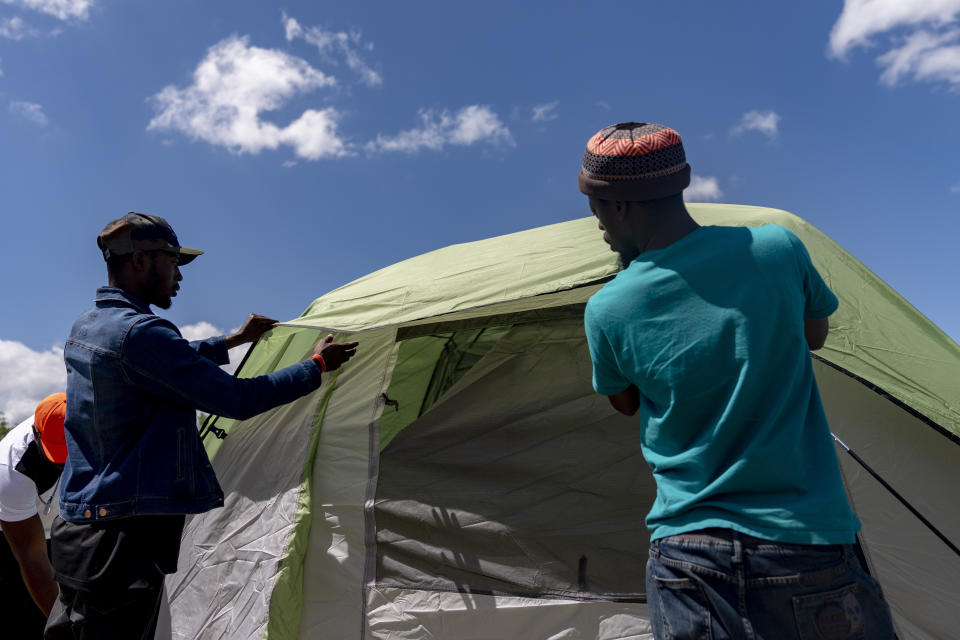 Asylum-seekers set up a tent at an encampment next to an unused motel owned by the county, Wednesday, June 5, 2024, in Kent, Washington. The group of about 240 asylum-seekers is asking to use the motel as temporary housing while they look for jobs and longer-term accommodations. (AP Photo/Lindsey Wasson)