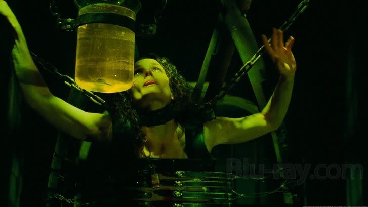 a woman is hanging, suspended in a jigsaw trap with a jar of liquid in front o f her in a scene from saw iii