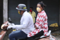 A motorist drives past a vendor wearing face mask and selling bananas outside a wholesale fruit market in Bengaluru, India, Saturday, May 30, 2020. India started easing lockdown restrictions earlier this month, allowing reopening of shops and manufacturing and resumption of some trains and domestic flights and vehicles' movement. The federal government is expected to issue a new set of guidelines this weekend, possibly extending the lockdown in worst-hit areas. (AP Photo/Aijaz Rahi)