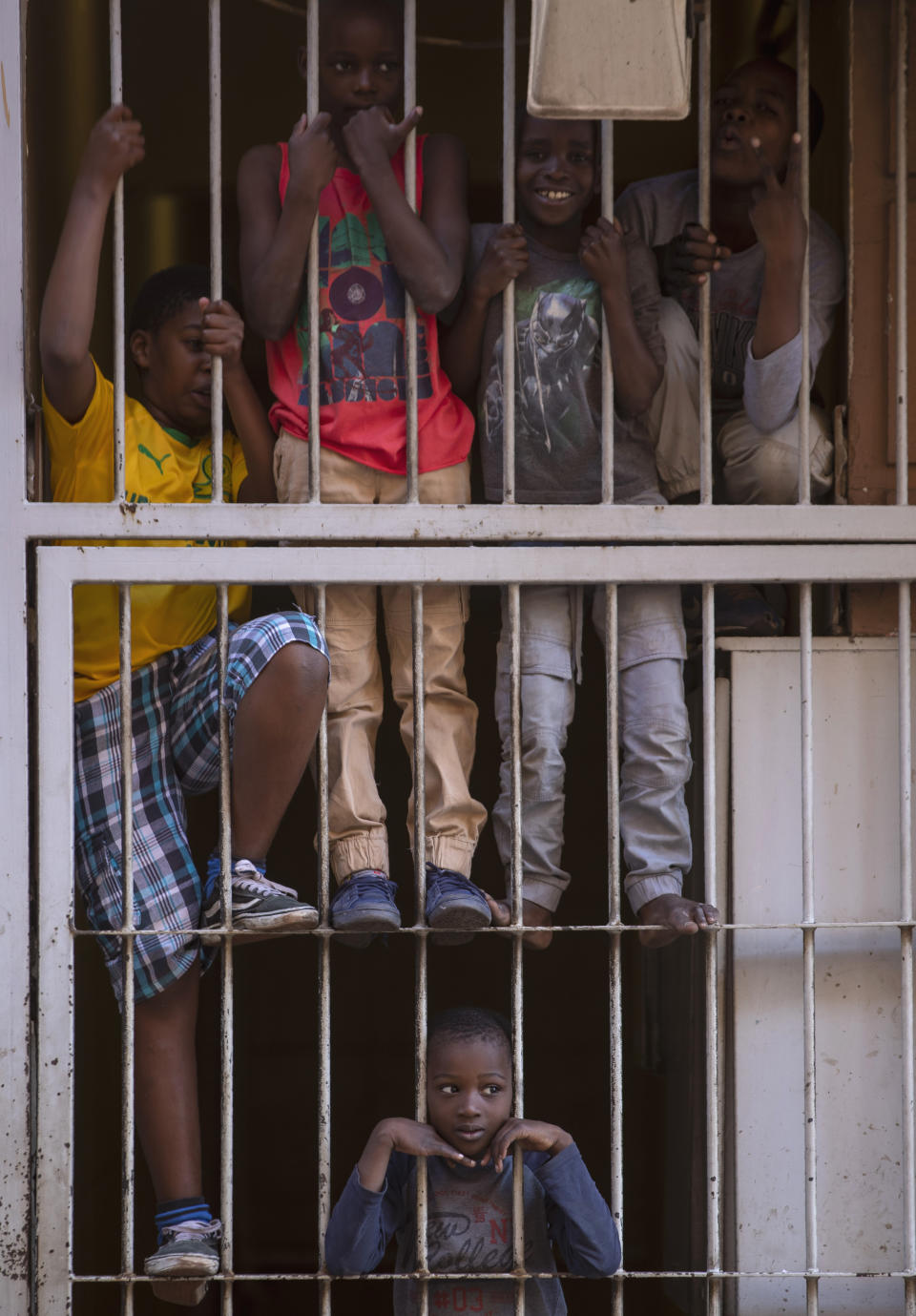 Children look out from a security gate of their flat, during a lockdown to help curb the spread of the new coronavirus in Johannesburg, South Africa, Tuesday, April 7, 2020. South Africa and more than half of Africa's 54 countries have imposed lockdowns, curfews, travel bans or other restrictions to try to contain the spread of COVID-19. The new coronavirus causes mild or moderate symptoms for most people, but for some, especially older adults and people with existing health problems, it can cause more severe illness or death. (AP Photo/Themba Hadebe)