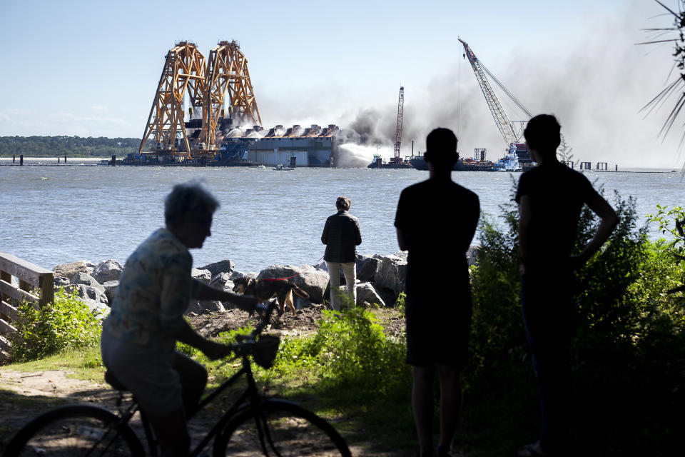 Residents watch firefighters hose down the hull of the overturned cargo ship Golden Ray, Friday, May 14, 2021, in Brunswick, Ga. The Golden Ray had roughly 4,200 vehicles in its cargo decks when it capsized off St. Simons Island south of Savannah, on Sept. 8, 2019. (AP Photo/Stephen B. Morton)