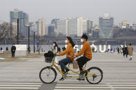 A couple wearing face masks rides a bicycle at a park in Seoul, South Korea, Saturday, March 7, 2020. The number of infections of the COVID-19 disease spread around the globe. (AP Photo/Ahn Young-joon)