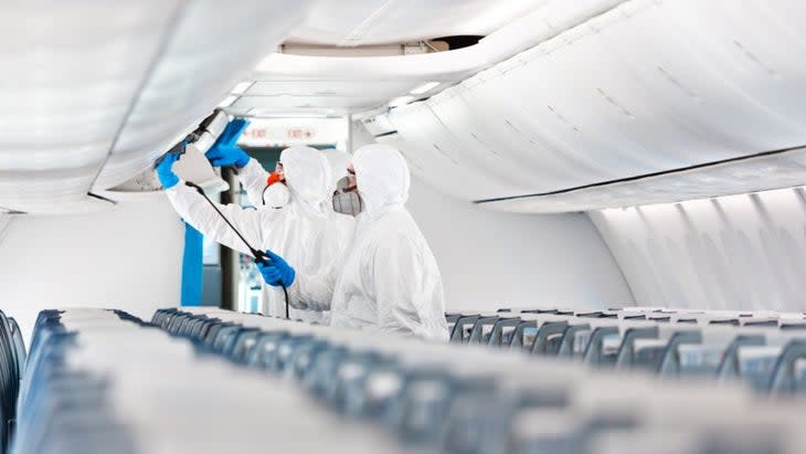 Three men dressed in what look like hazmat suits and gloves, disinfecting the inside of a plane during the COVID pandemic