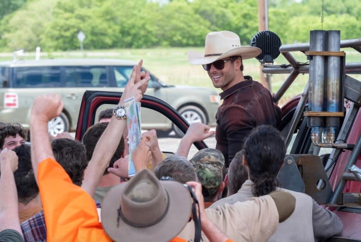 Glen Powell stands on a truck and smiles in Twisters.