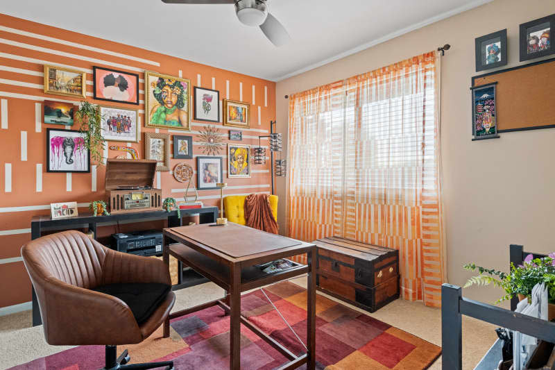 Office with orange and white gallery wall, orange and white curtains, and wood desk with brown leather task chair