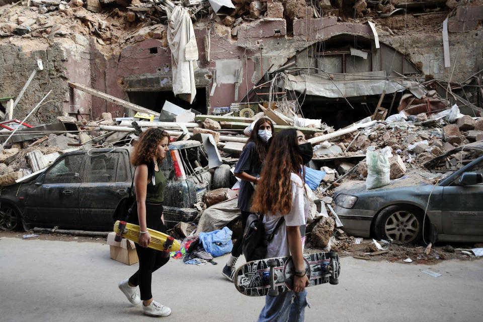 Un grupo de mujeres pasa por delante de autos destrozados en un vecindario próximo al lugar donde se registró una potente explosión, en Beirut, Líbano, el 7 de agosto de 2020. (AP Foto/Thibault Camus)