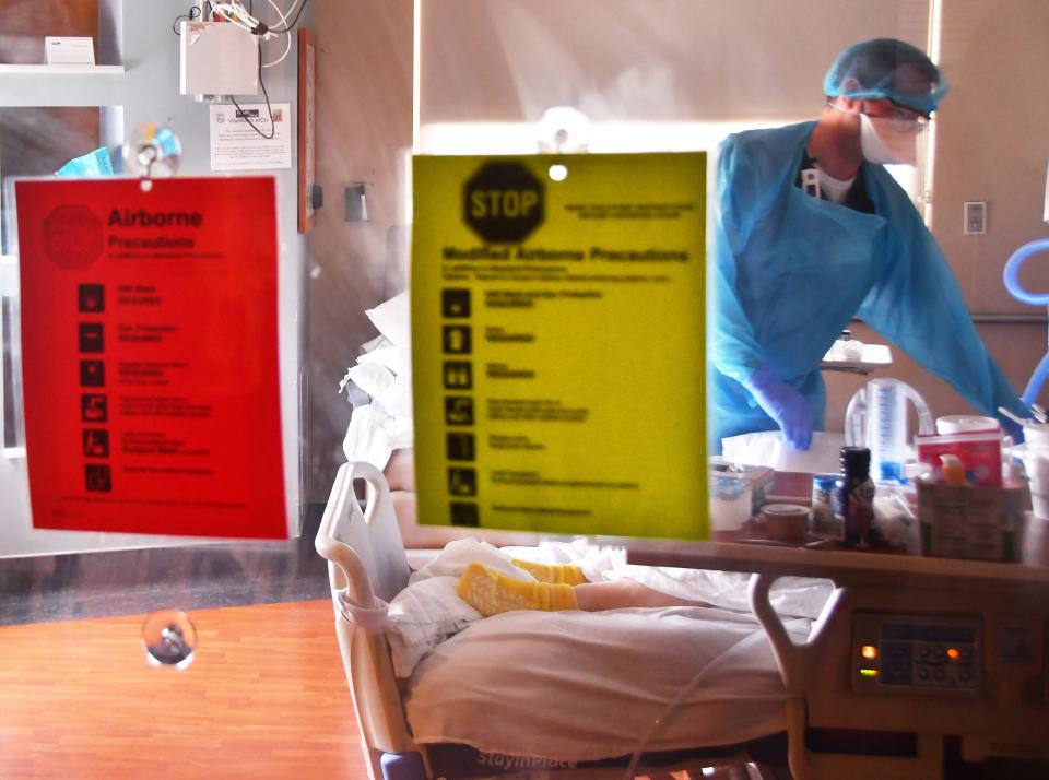 Seen through a protective glass door, Dustin Evans, a critical care nurse,  attends to a COVID patient in the I.C.U. unit on the 4th floor of Holmes Regional Medical Center.  