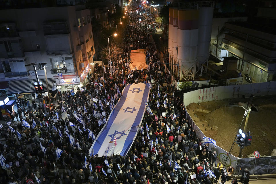 Israelis march with large national flag during a protest against plans by Prime Minister Benjamin Netanyahu's new government to overhaul the judicial system, in Tel Aviv, Israel, Saturday, Feb. 18, 2023. (AP Photo/Tsafrir Abayov)