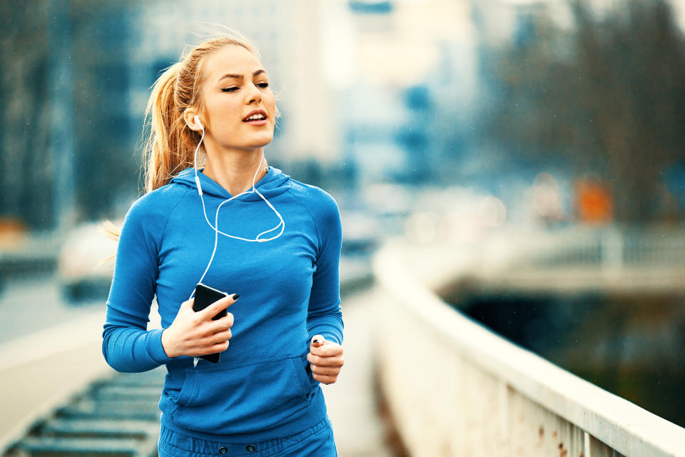 Happy Young Woman Listening Music While Jogging On Bridge